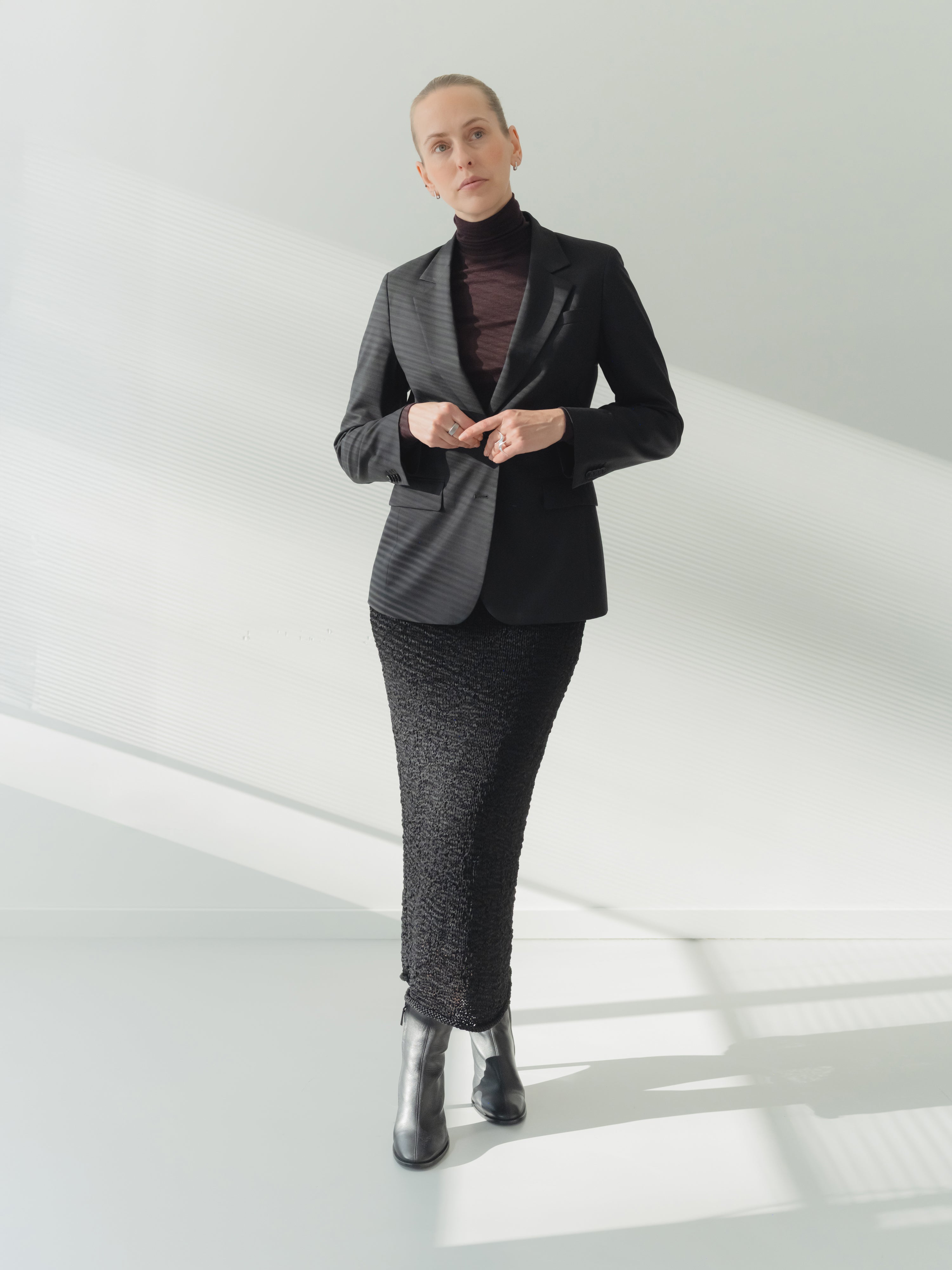 Single-breasted women’s black stretch wool fine twill blazer with notch lapel styled with a skirt.