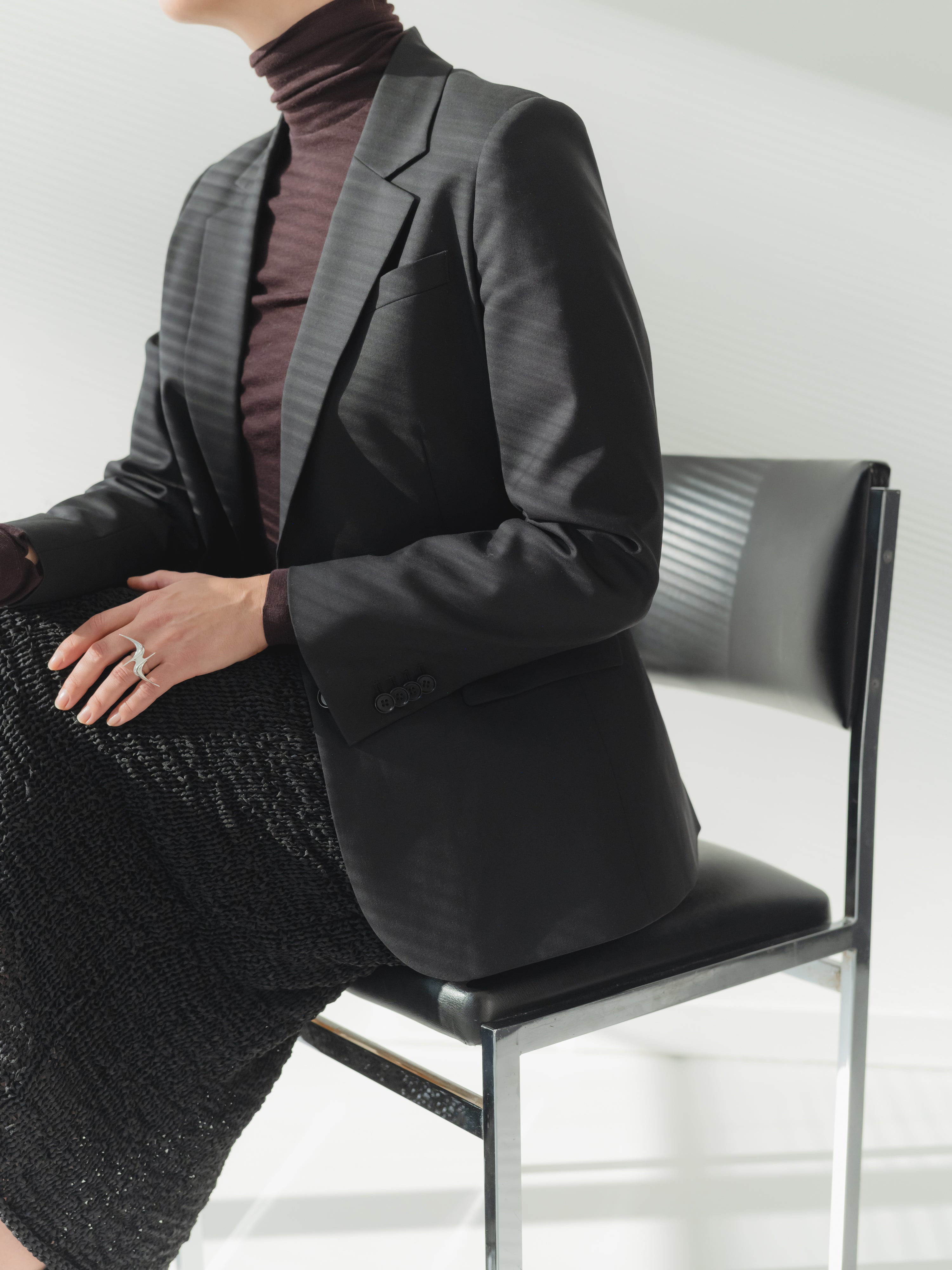 Single-breasted women’s black stretch wool fine twill blazer with notch lapel styled with a skirt.