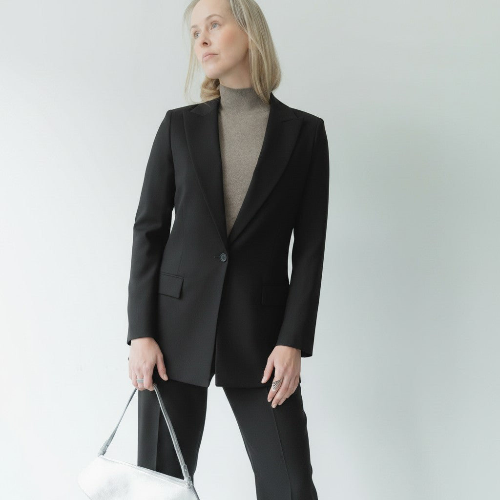 NOVEM STUDIO navy blue wool blend suit with peak lapel blazer and straight-leg trousers. Model holds a silver handbag.